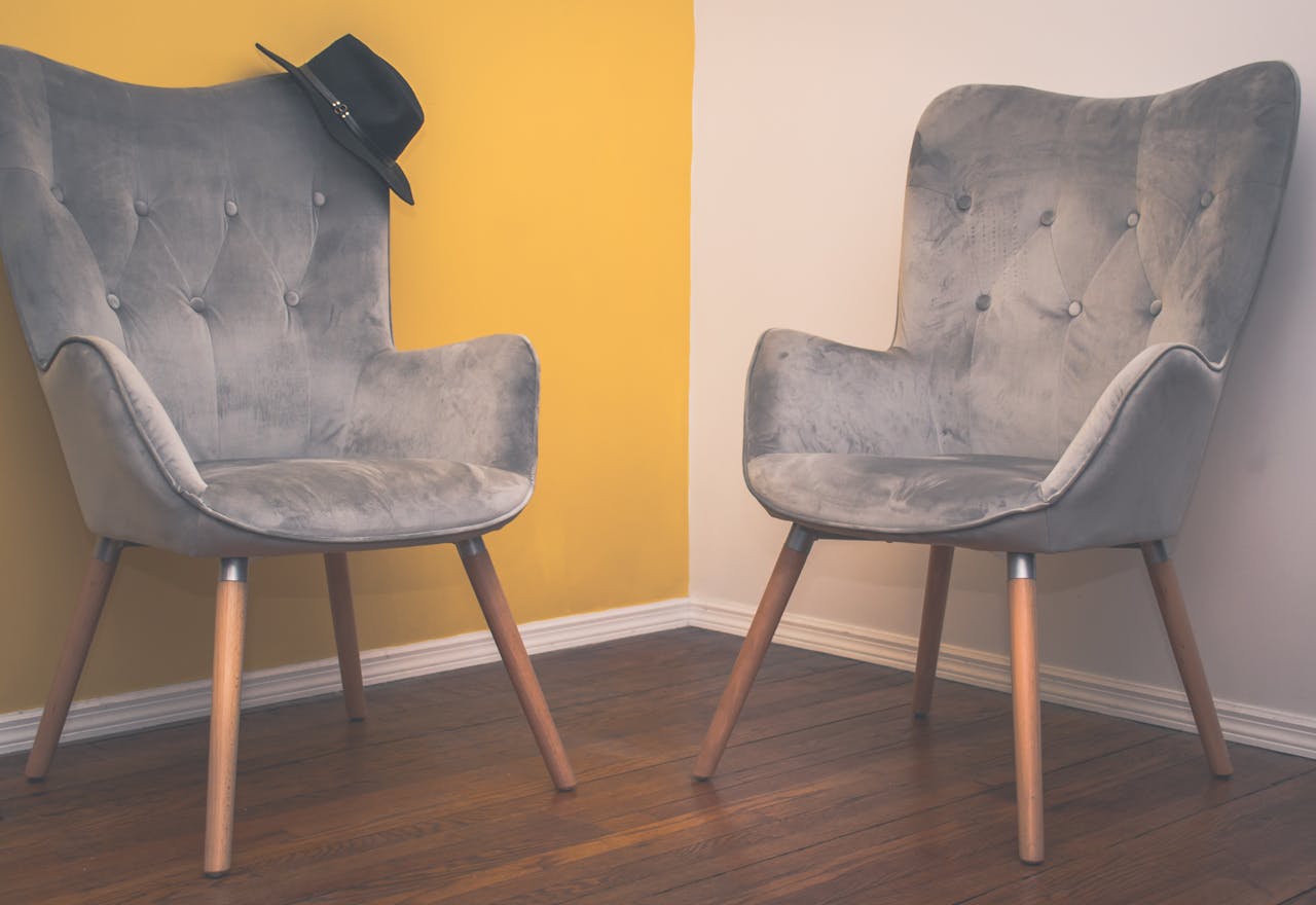 about-01 Two contemporary gray armchairs in a minimalist interior with a yellow accent wall and wooden flooring.